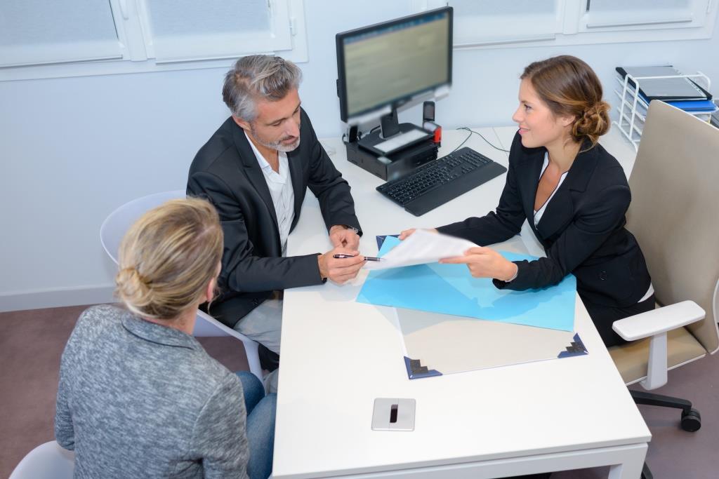 Image d'un notaire expliquant des documents à un couple lors d'une transaction immobilière.